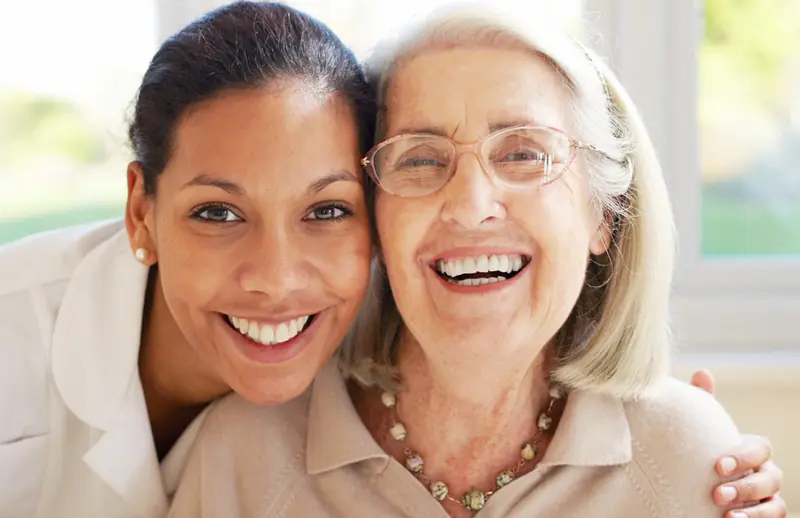 Caregiver and a smiling older woman posing cheek to cheek