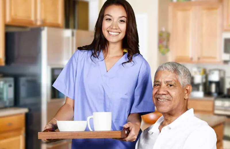 Caregiver bringing an older man a tray with coffee
