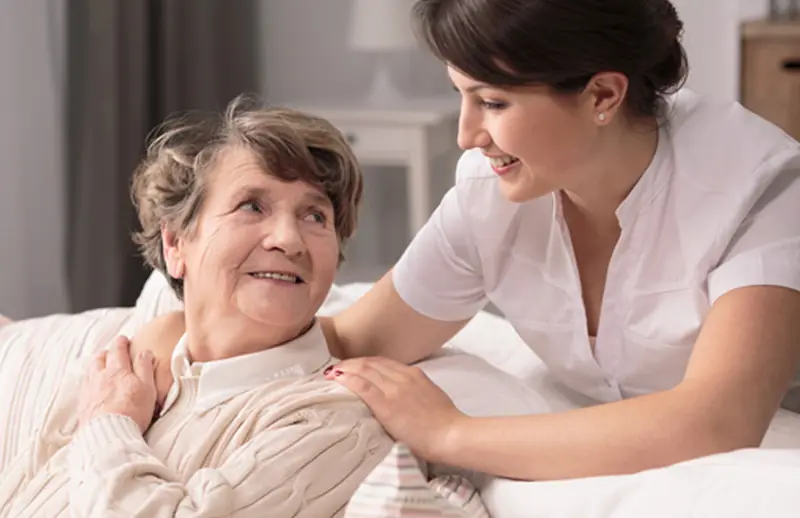 Caregiver helping an older woman sit up in bed